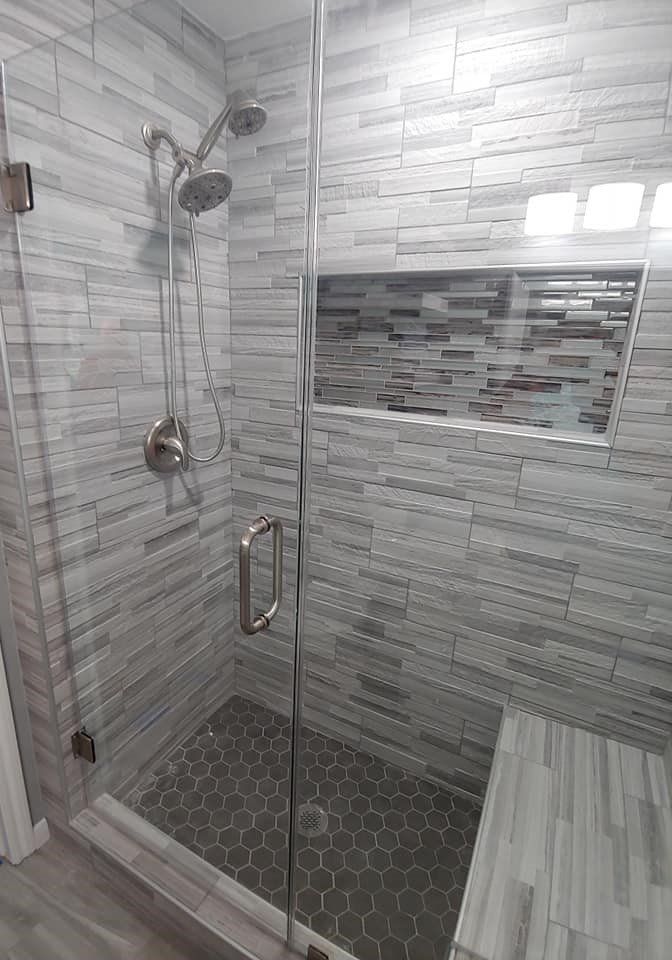 A bathroom with a walk in shower with a glass door and a bench.