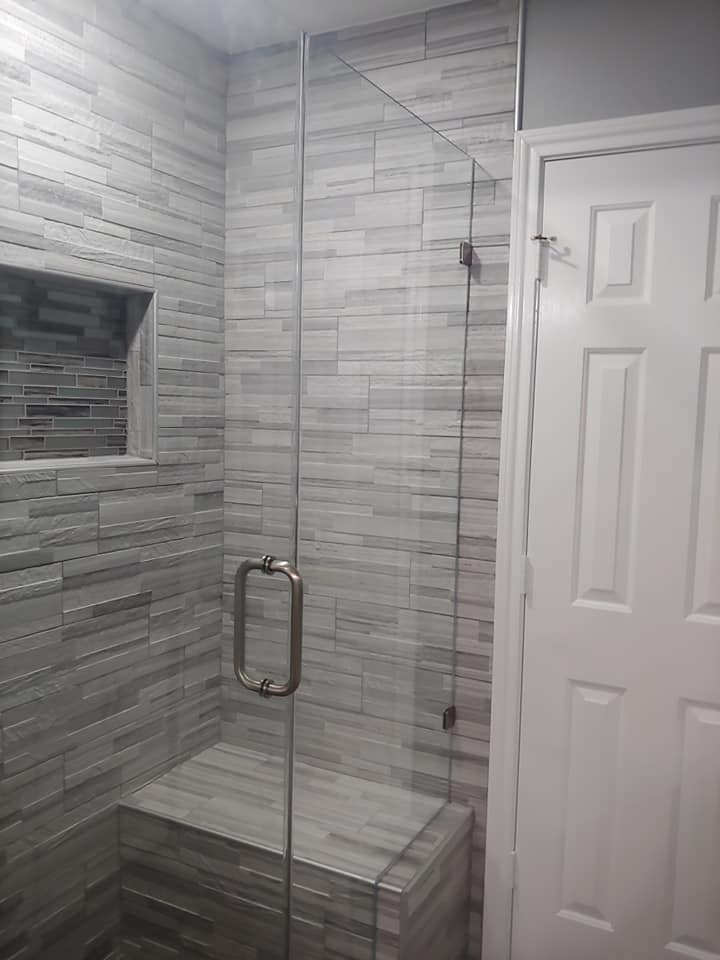 A bathroom with a glass shower door and a bench.