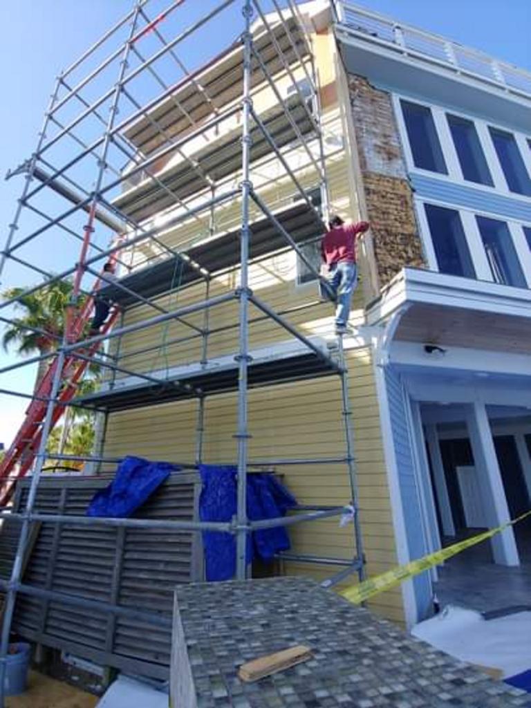 A man is painting the side of a house with scaffolding.
