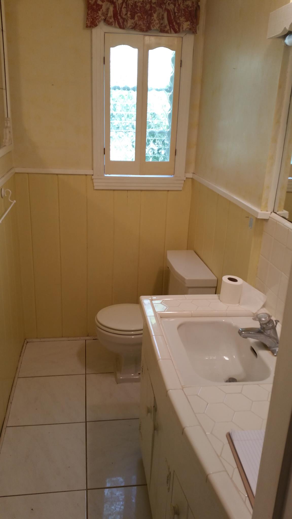 A bathroom with a toilet , sink , mirror and window.