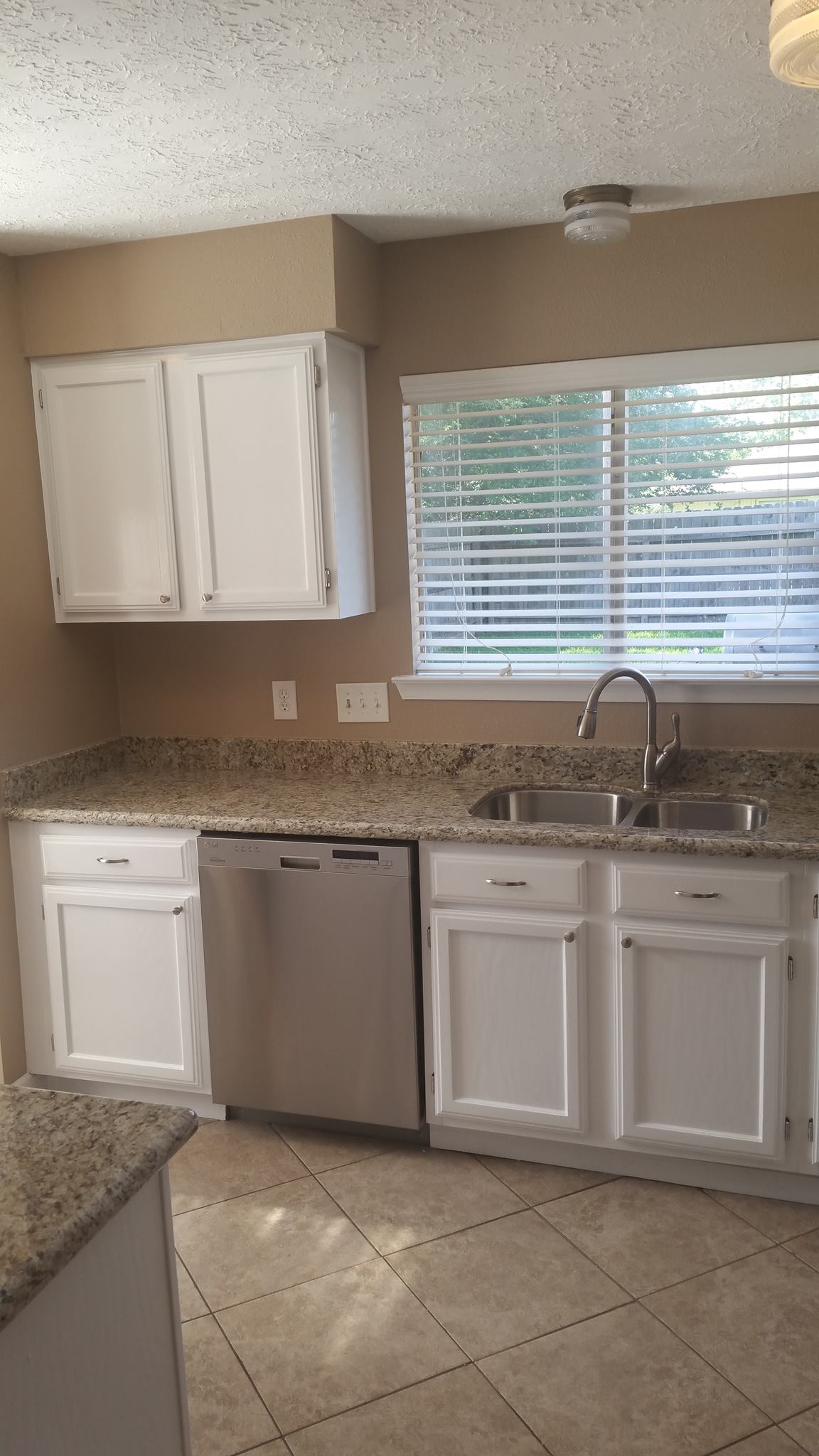 A kitchen with white cabinets , stainless steel appliances , a sink , and a window.