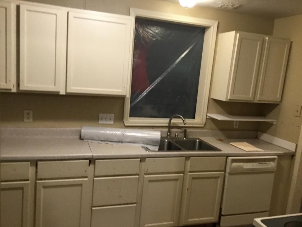A kitchen with white cabinets , a sink , and a window.