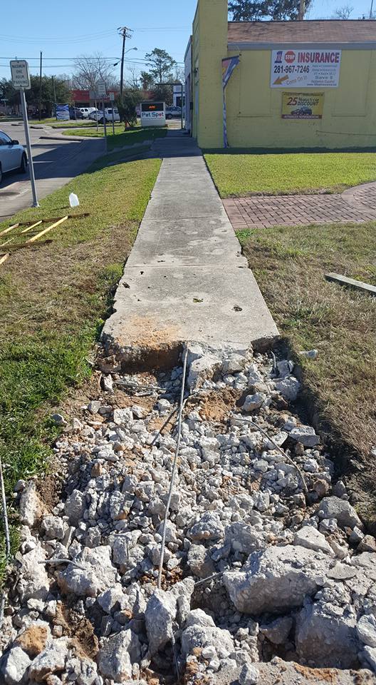 A sidewalk is being demolished in front of a yellow building.