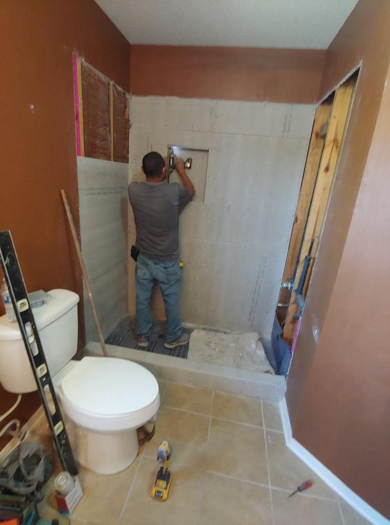 A man is standing in a bathroom next to a toilet and a level.