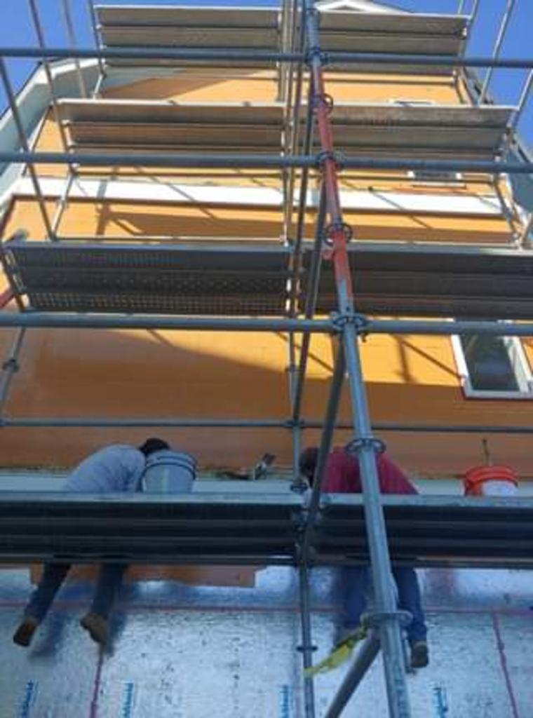 Two men are standing on scaffolding in front of a building.