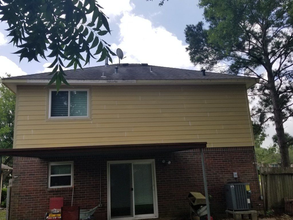 The back of a brick house with a yellow siding and a sliding glass door.