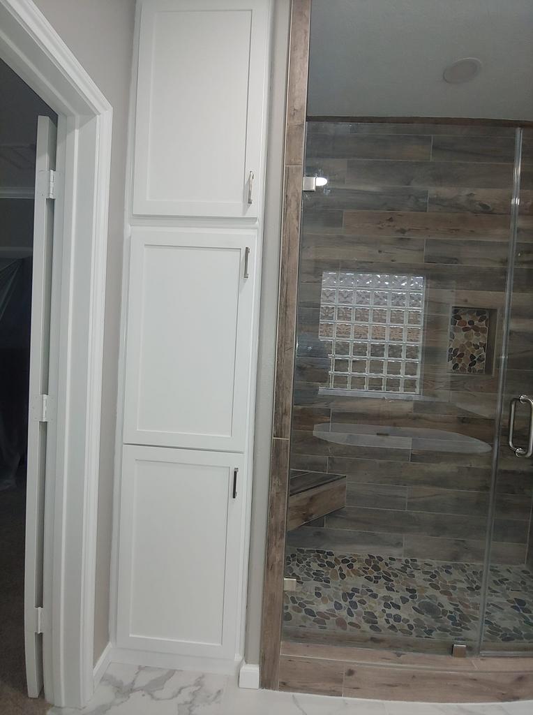A bathroom with a walk in shower and white cabinets.