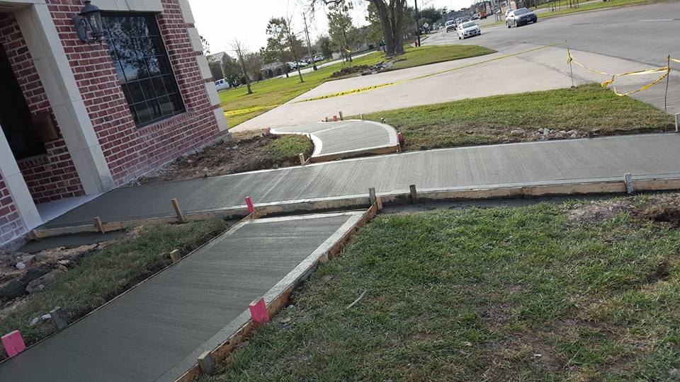 A concrete walkway is being built in front of a brick house.