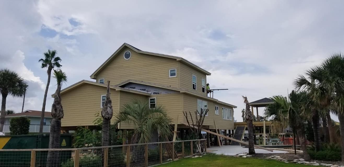 A large house is being built on stilts with palm trees in the background.
