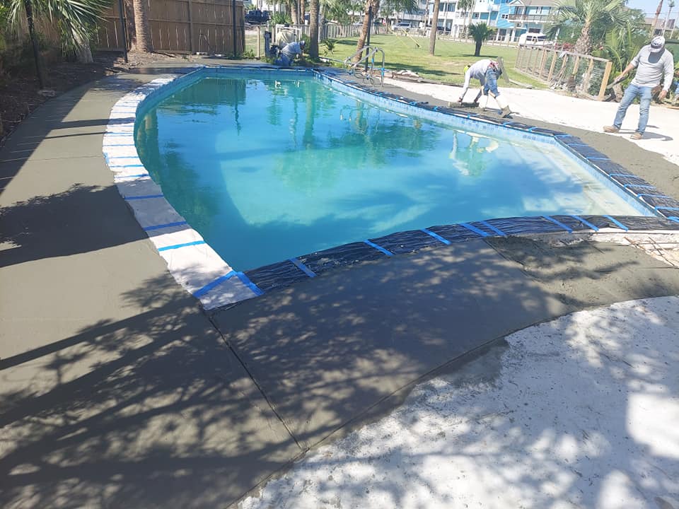 A man is laying concrete around a swimming pool.