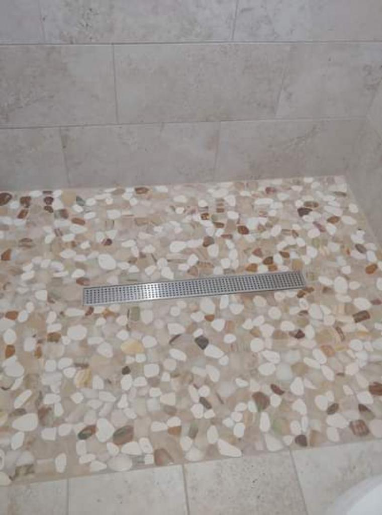 A walk in shower with a tiled floor and a drain.