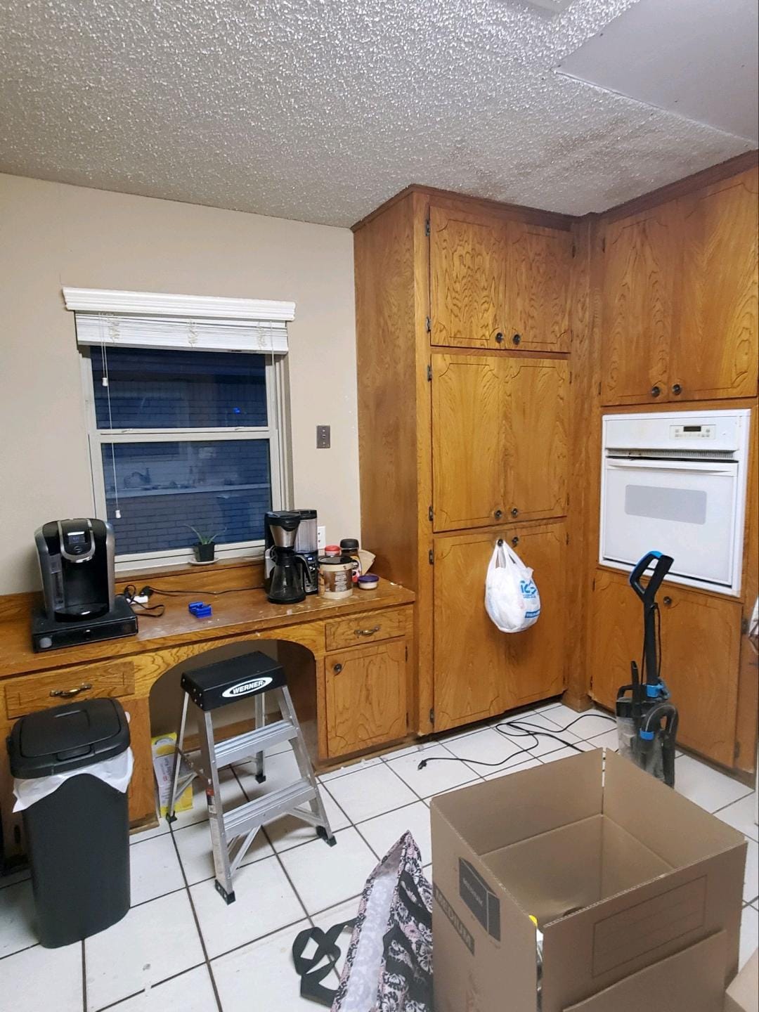 A kitchen with wooden cabinets , boxes , a trash can , and a window.