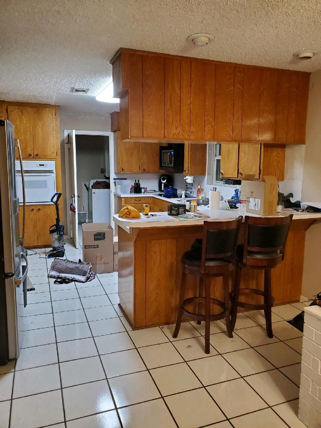 A kitchen with wooden cabinets and stools and a tiled floor.