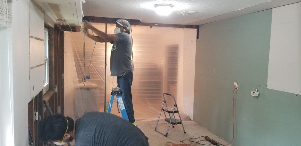 A couple of men are working on a wall in a room.
