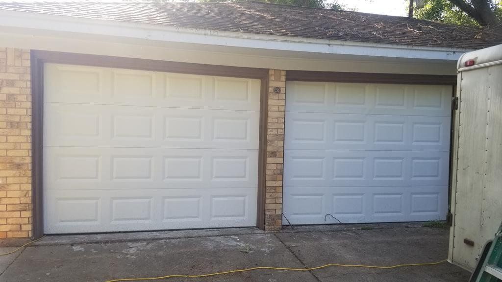 A pair of white garage doors on a brick house.