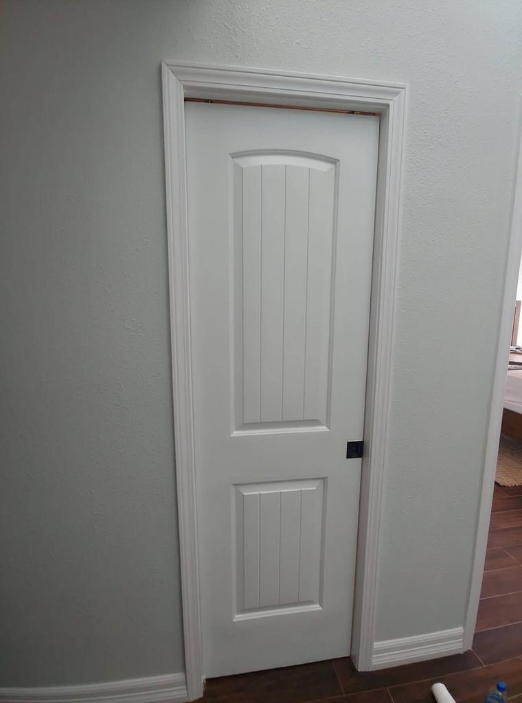 A white door with a black handle is in a hallway.