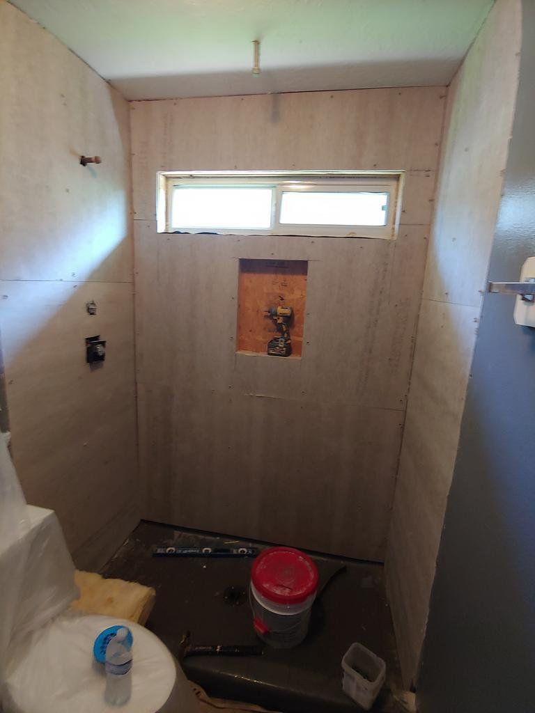 A bathroom under construction with a window and a bucket on the floor.