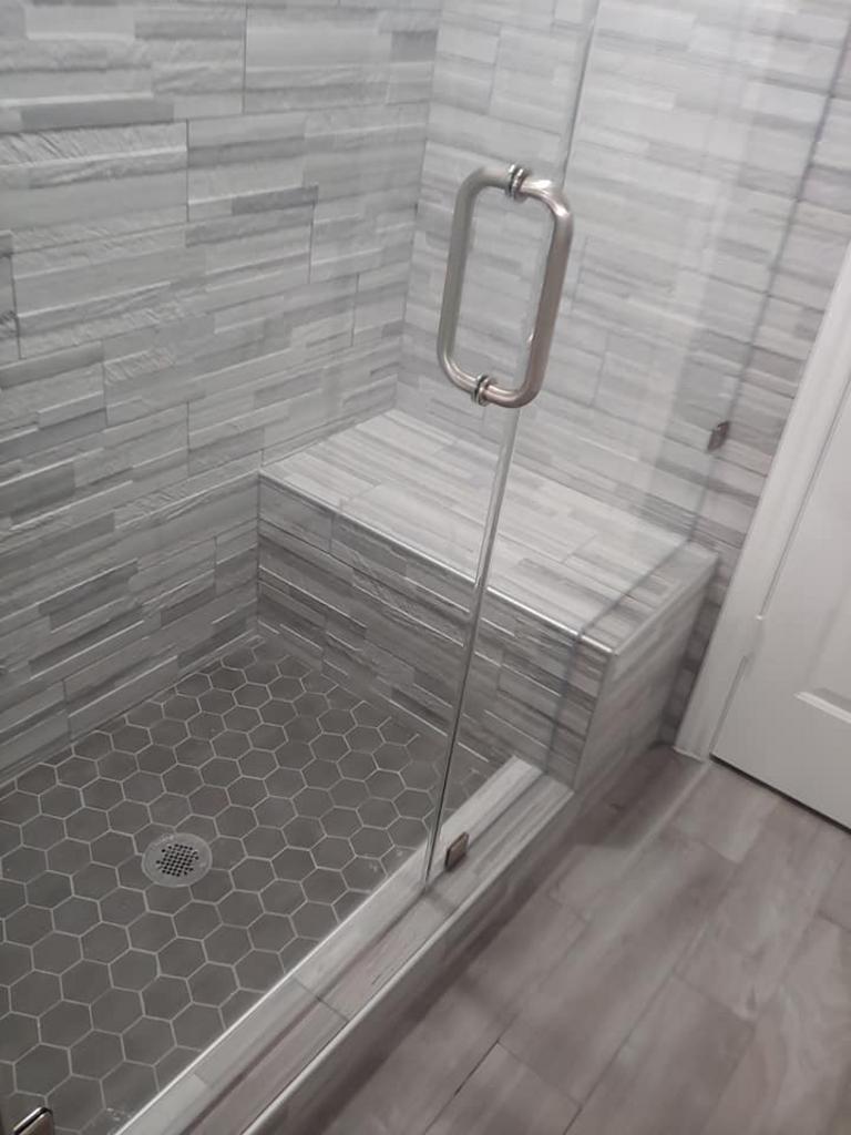 A shower with a glass door and a bench in it.