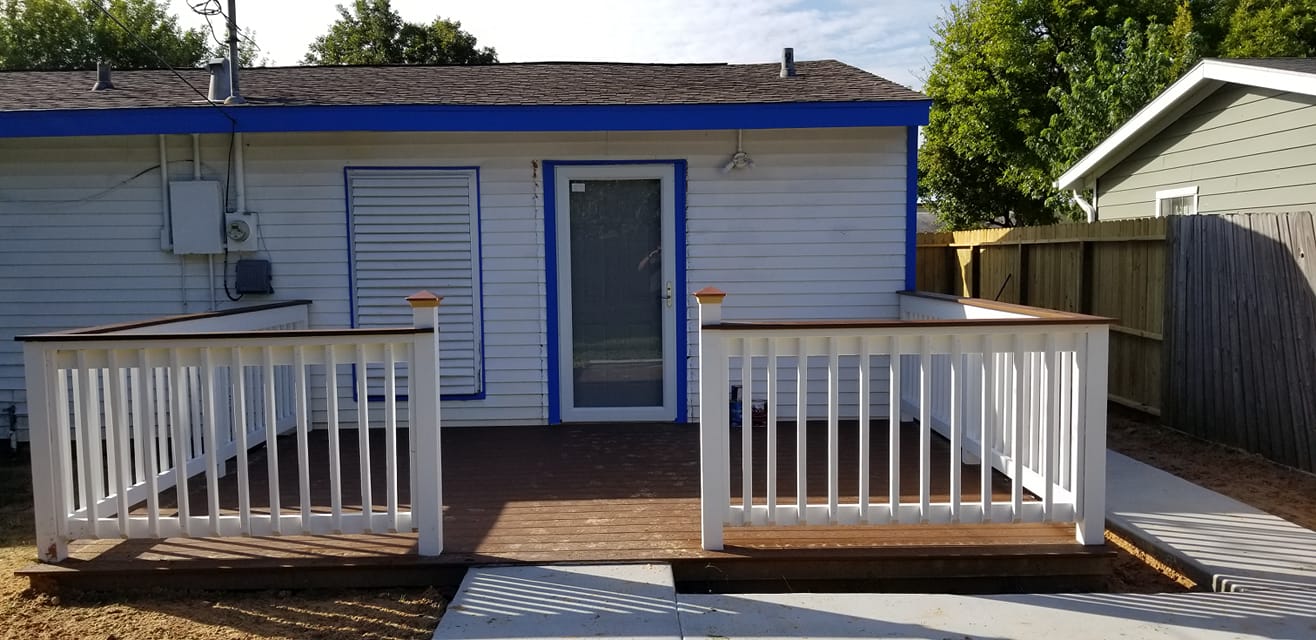 A white house with a blue trim and a deck in front of it.