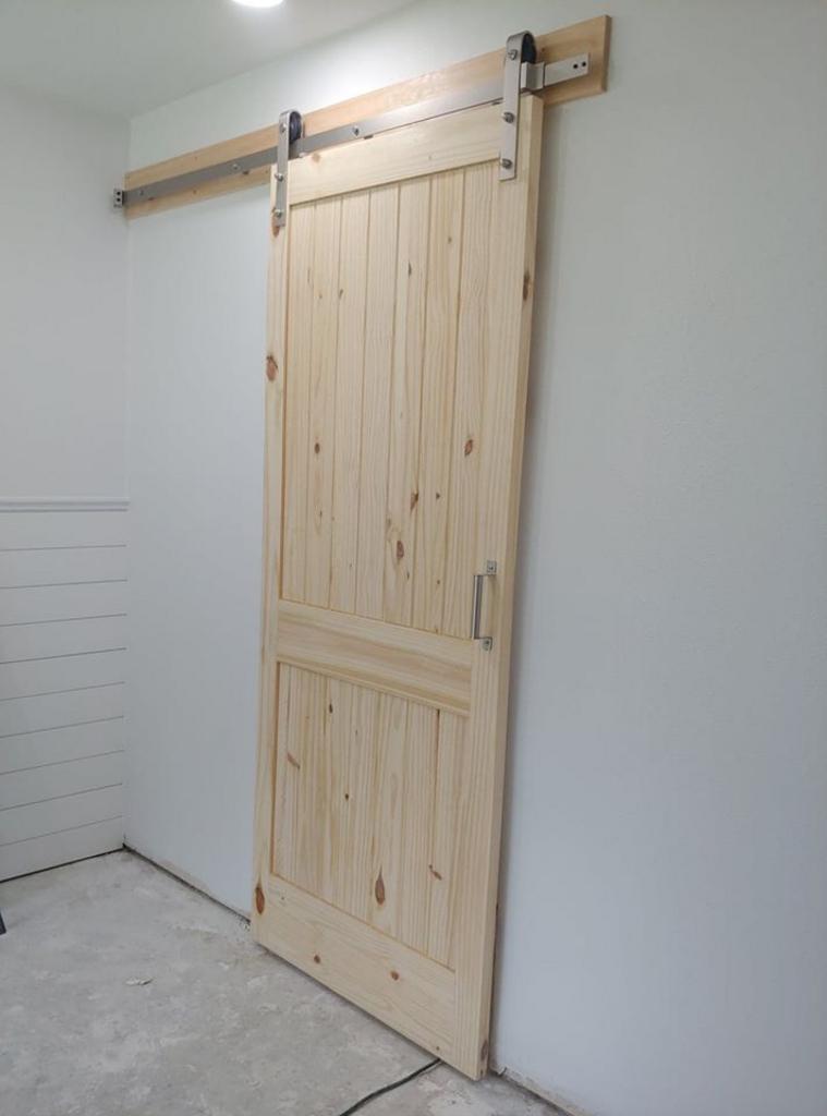 A wooden sliding barn door is hanging on a white wall.