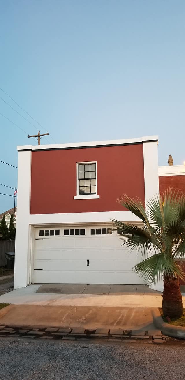 A red and white house with a white garage door and a palm tree in front of it.