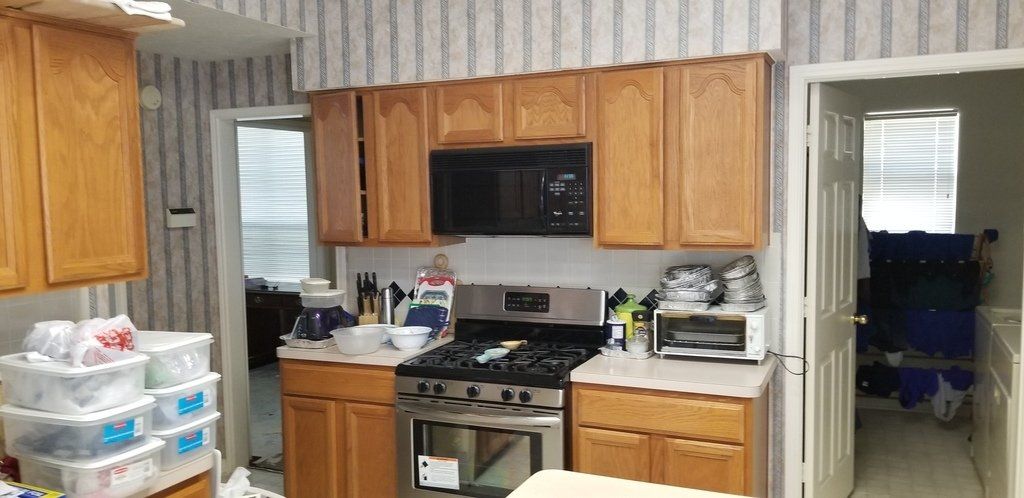 A kitchen with wooden cabinets , a stove , microwave , and refrigerator.