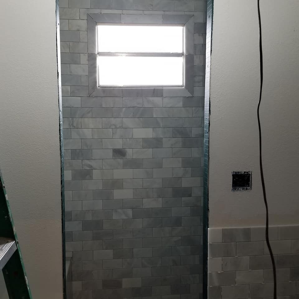 A bathroom with a tiled wall and a window.