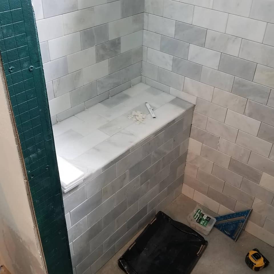 A bathroom with white tiles and a black tray on the floor.