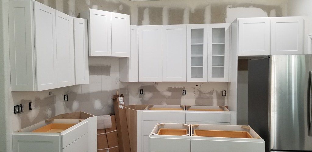 A kitchen under construction with white cabinets and a stainless steel refrigerator.
