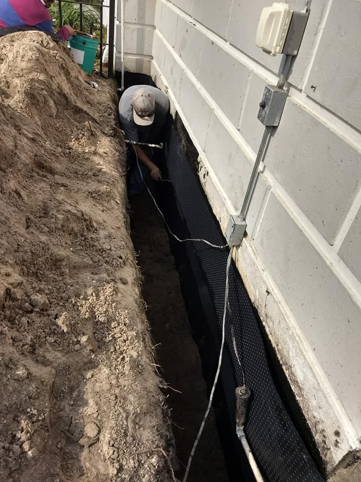 A man is digging a hole in the ground next to a brick wall.