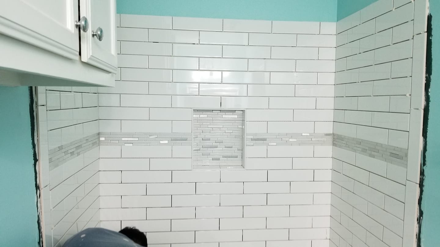 A man is laying on the floor in a bathroom with white tiles.