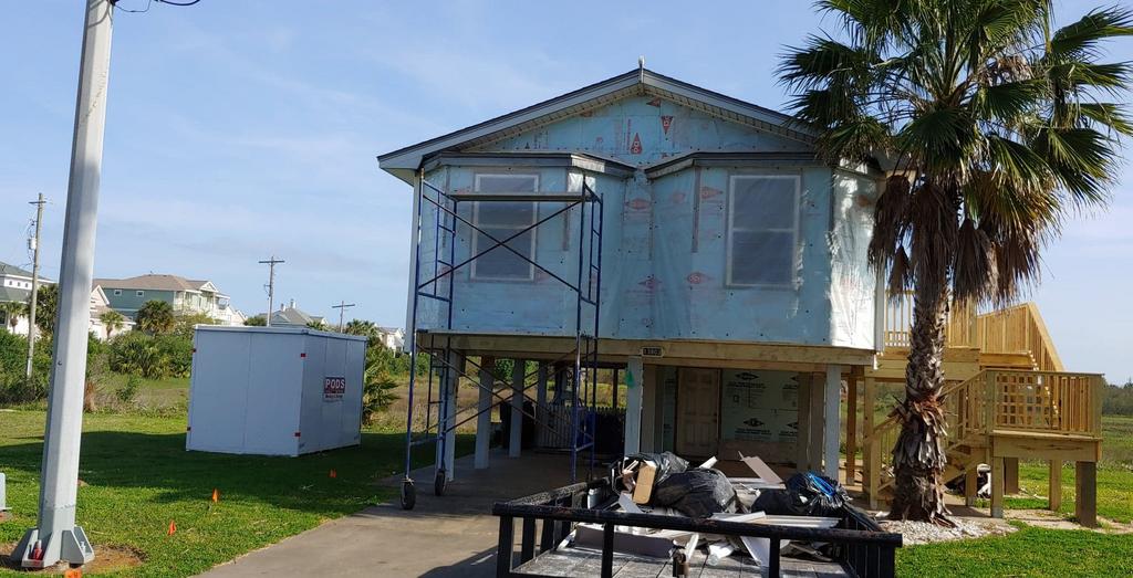 A blue house is being built on stilts with a palm tree in front of it.