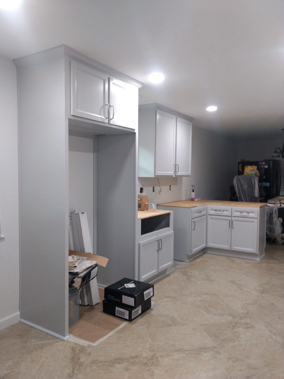 A kitchen with white cabinets and wooden counter tops is being remodeled in a basement.