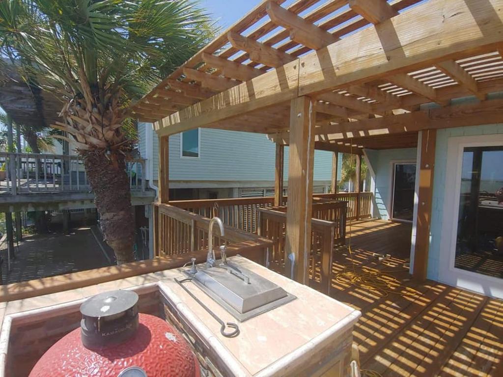 A large red grill is sitting under a wooden pergola on a deck.