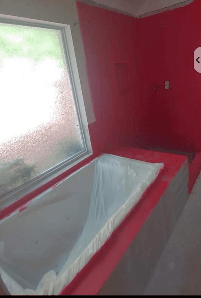 A bathtub in a bathroom with red walls and a window.