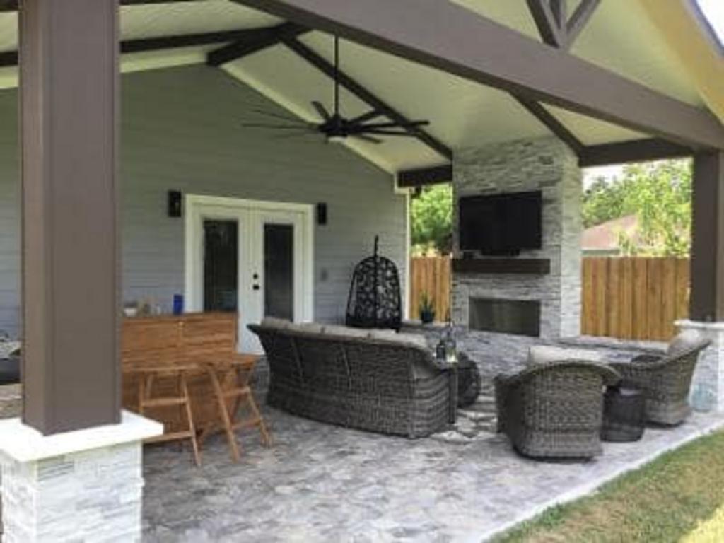 A patio with a fireplace , couch , chairs and a television.