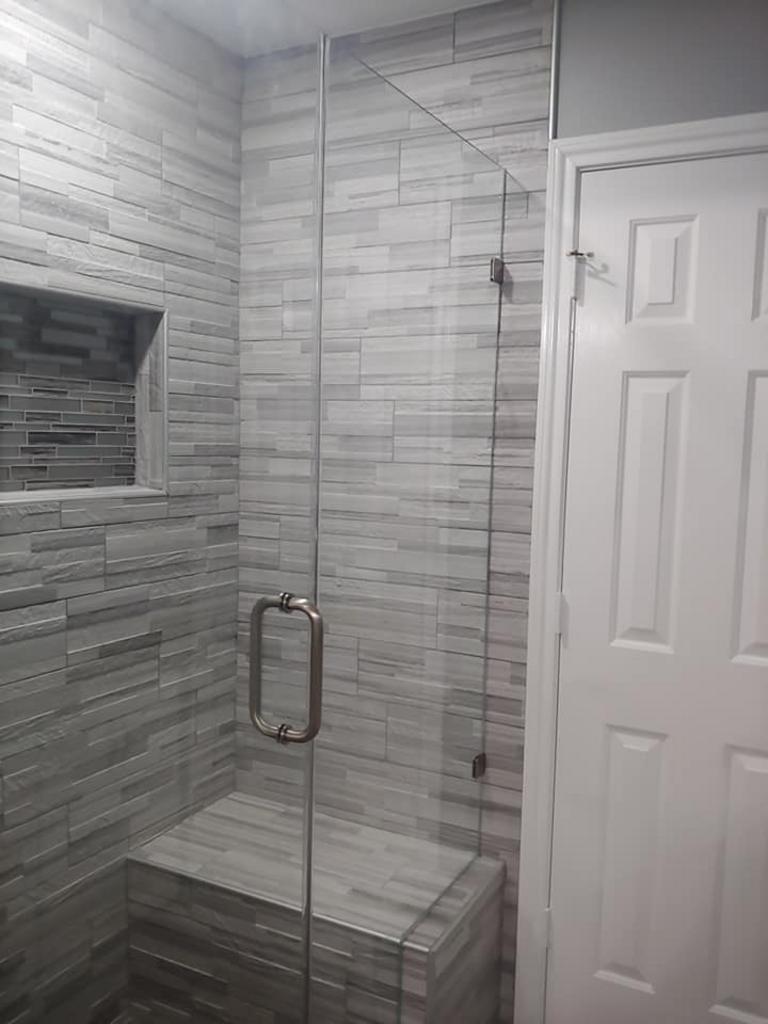 A bathroom with a glass shower door and a bench.
