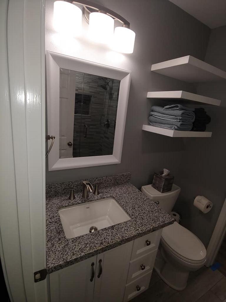 A bathroom with a sink , toilet , mirror and shelves.