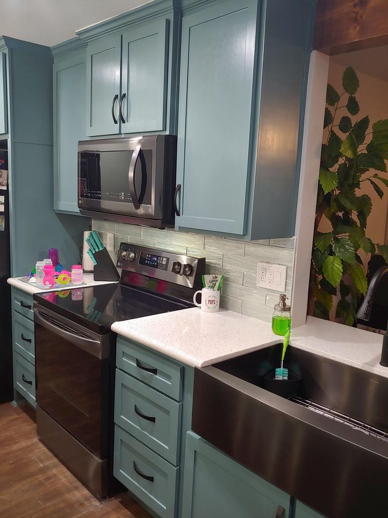 A kitchen with blue cabinets , stainless steel appliances , a sink and a microwave.