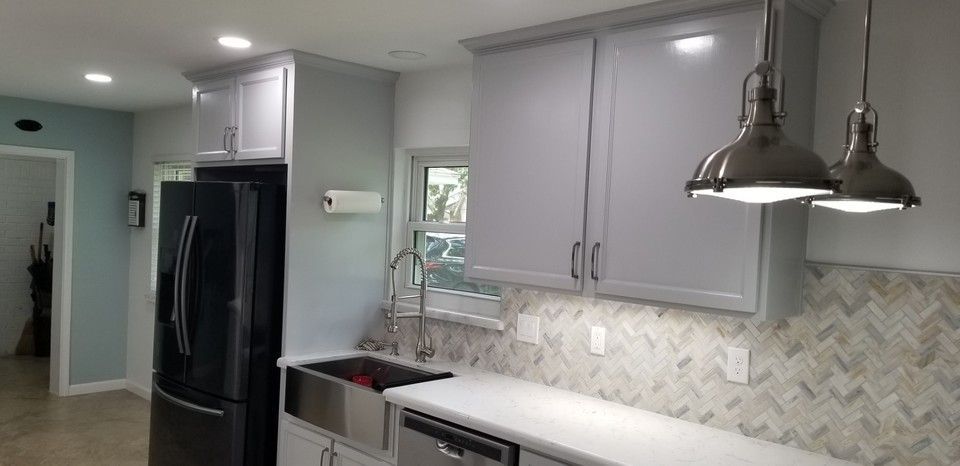 A kitchen with gray cabinets , a black refrigerator , a sink , and a window.