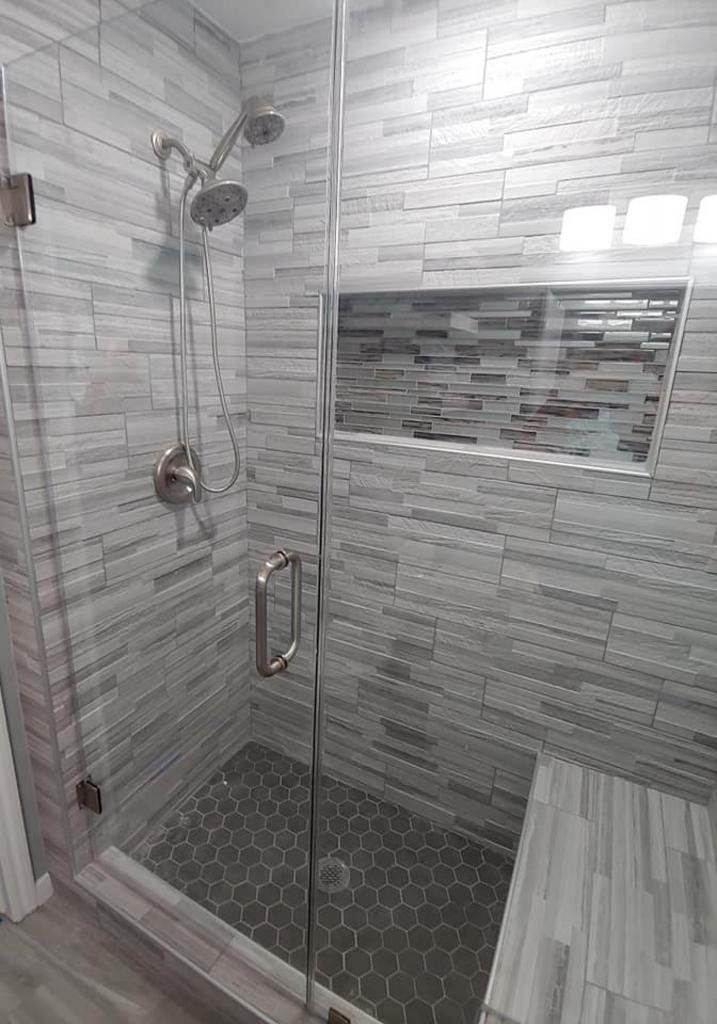 A bathroom with a walk in shower with a glass door and a bench.