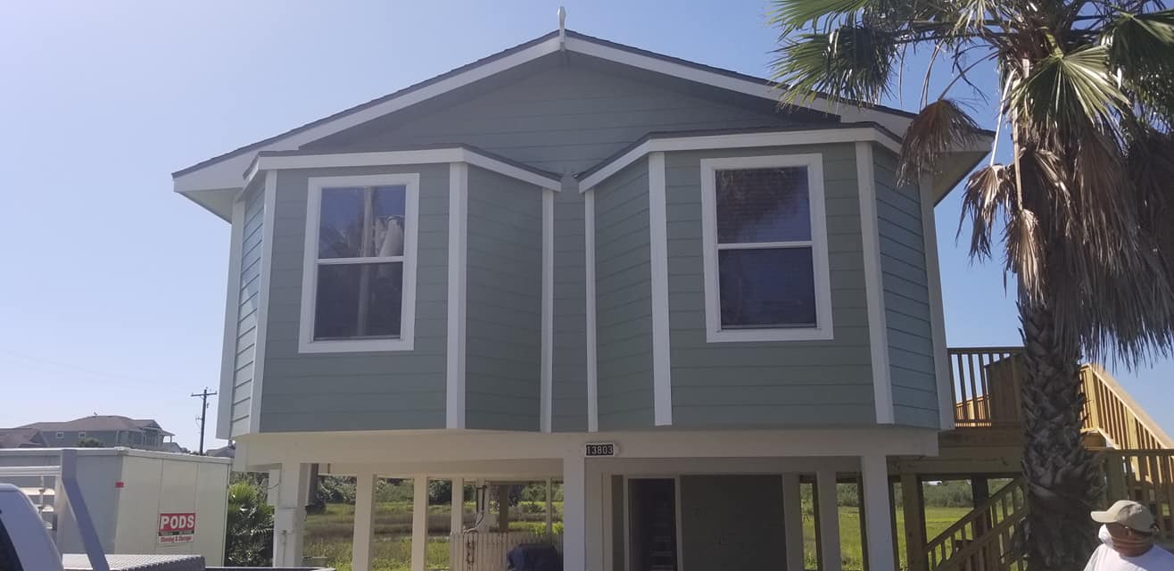 A man in a cowboy hat is standing in front of a green house.