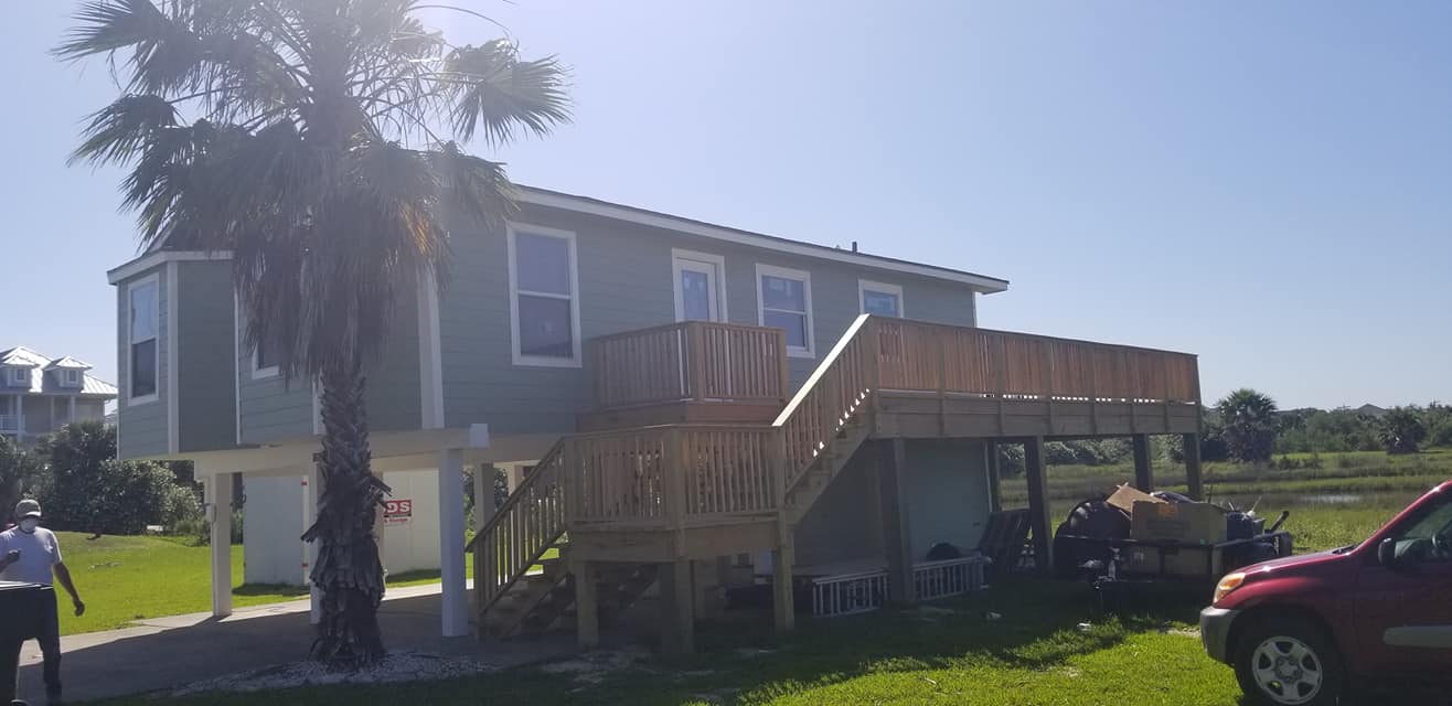 A house with a large deck and stairs is sitting on top of a lush green field.