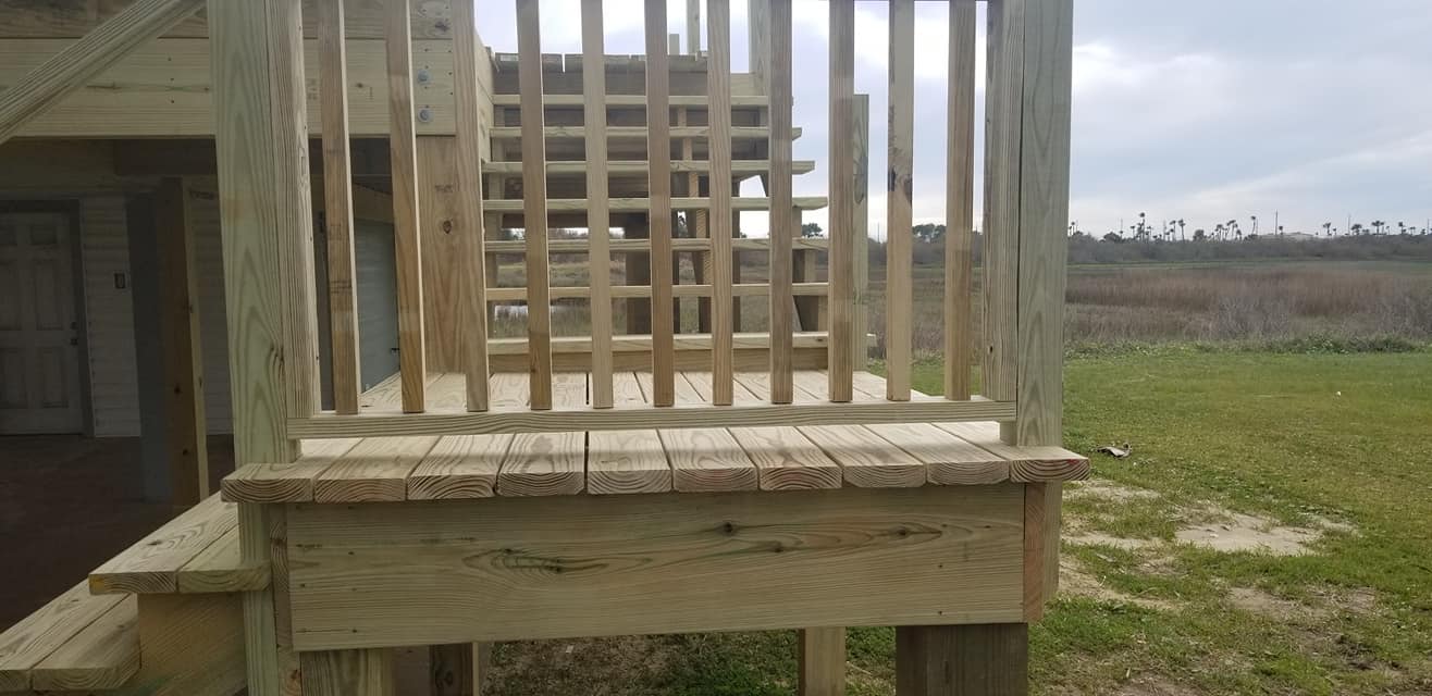 A wooden deck with stairs and a railing in a grassy field.
