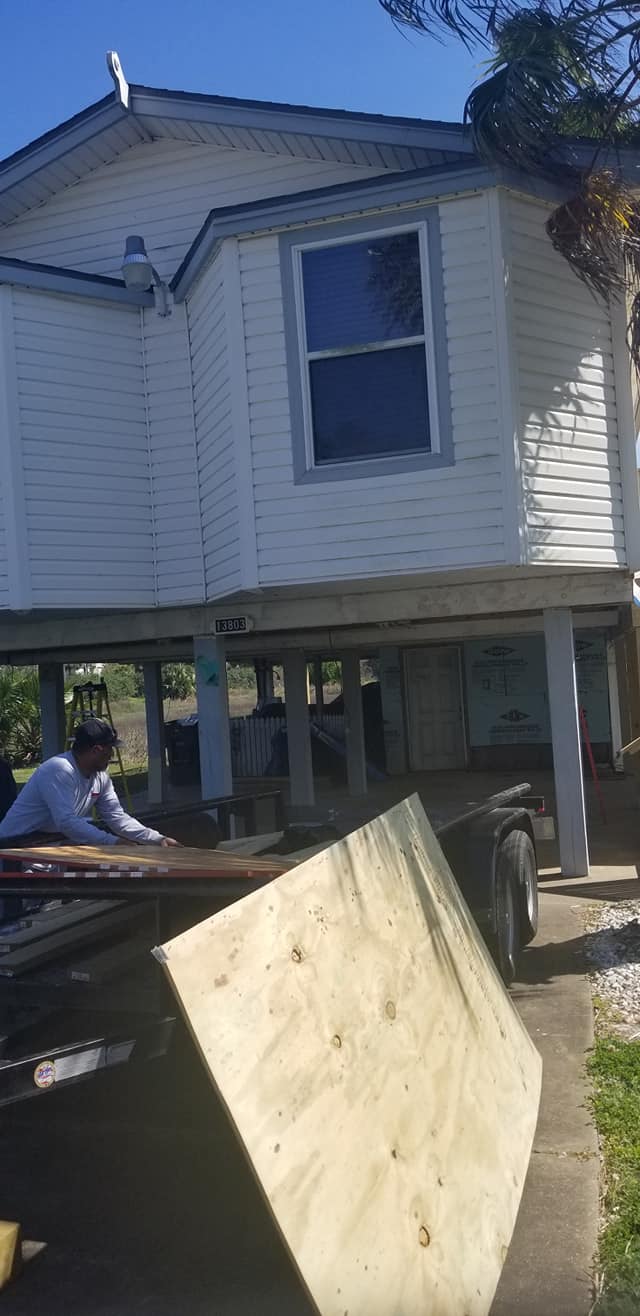 A man is sitting on a truck in front of a house.