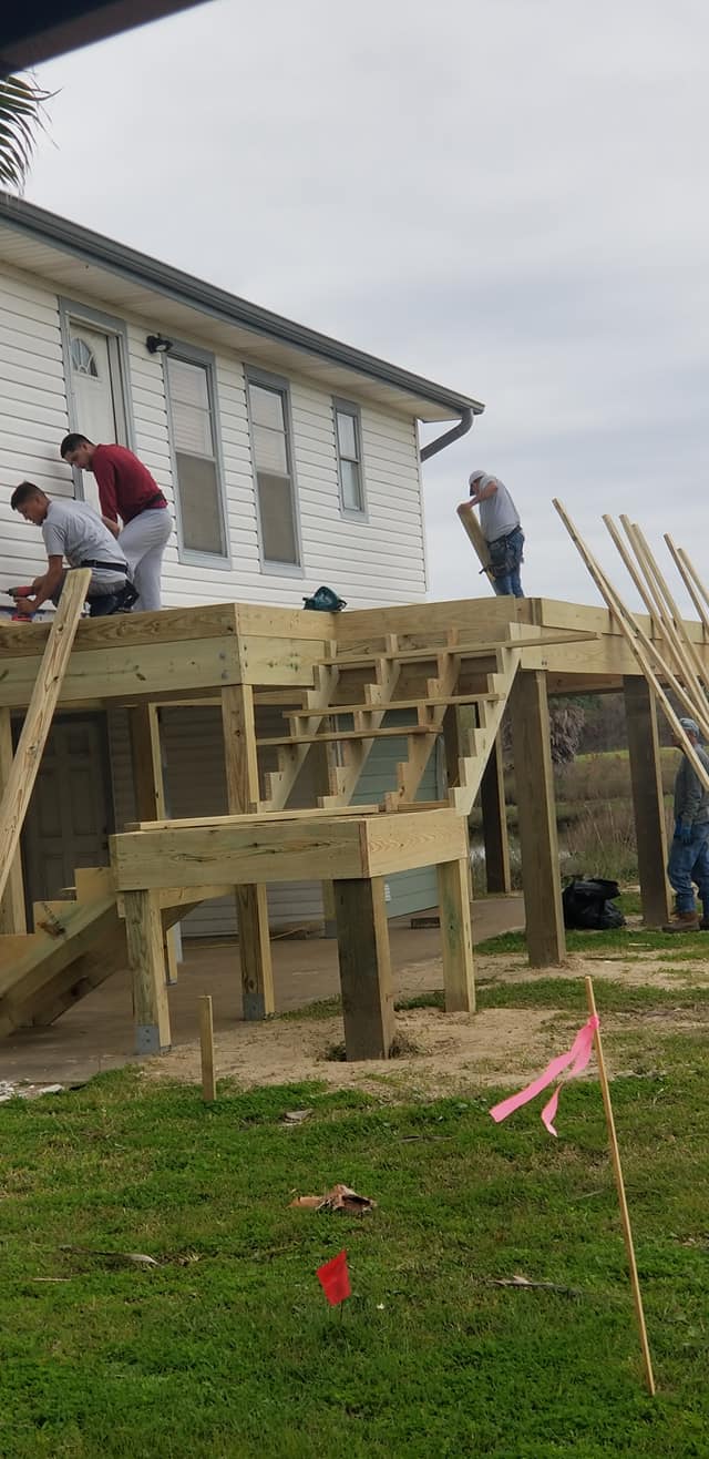 A group of people are working on a wooden deck in front of a house.