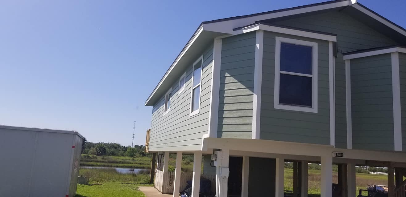 A green house on stilts with a blue sky in the background.