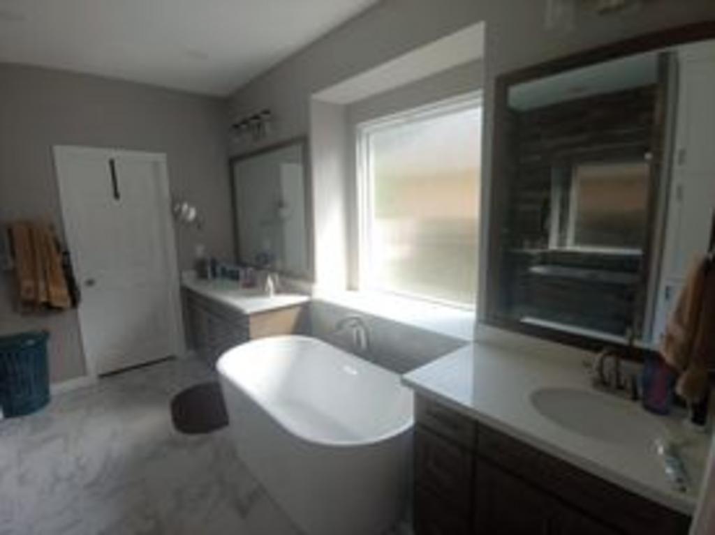 A bathroom with a tub , sink , mirror and window.