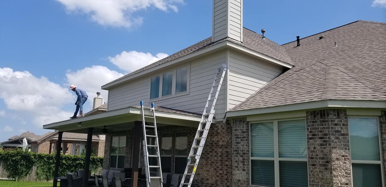 A man is standing on the roof of a house with a ladder.