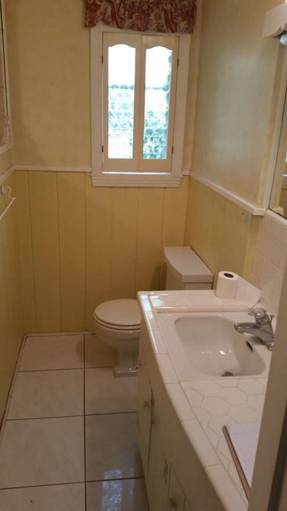 A bathroom with a toilet , sink , mirror and window.